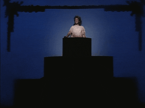 a woman in a white dress stands on a podium in a dark room
