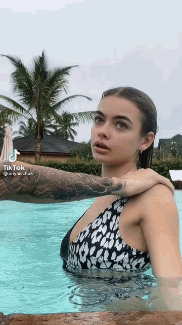 a woman in a bikini is swimming in a pool and has a tattoo on her arm .