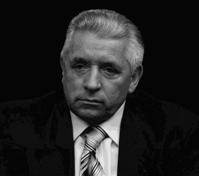 a man in a suit and tie sits in front of a wall