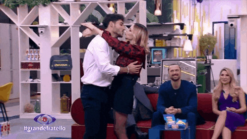 a man and woman are kissing in front of a sign that says #grandefratello