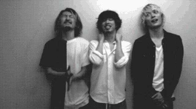 three men are standing next to each other and one has his hand on his face