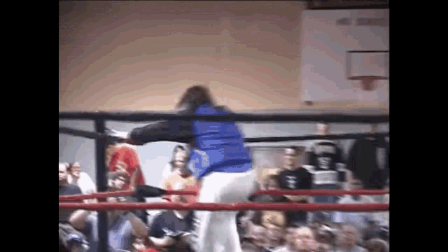 a man in a blue jacket is standing in a boxing ring with a crowd watching