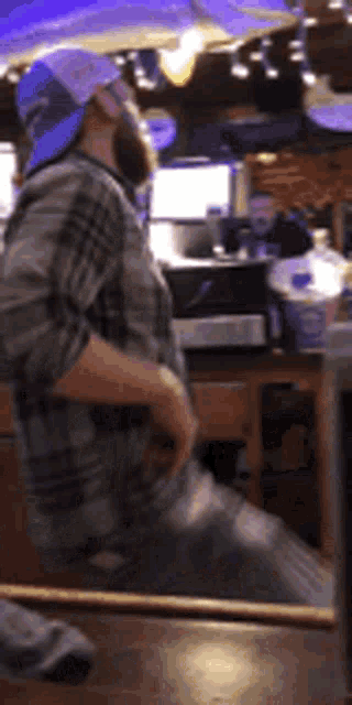 a man in a plaid shirt and a blue hat is dancing in a bar