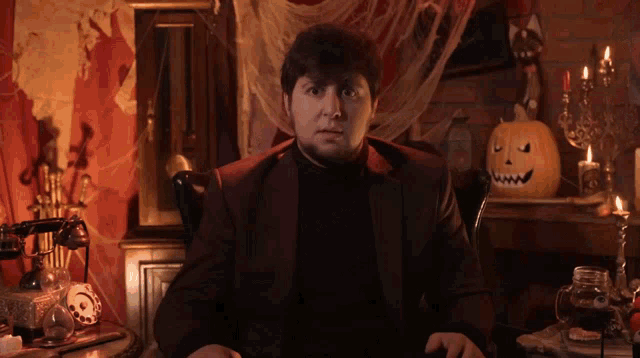 a man in a suit sits in front of a table with a pumpkin and candles on it