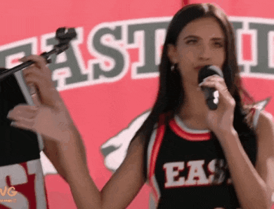 a woman is singing into a microphone while wearing a east jersey