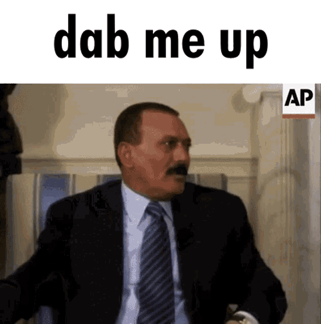 a man in a suit and tie is sitting in front of a sign that says " dab me up "