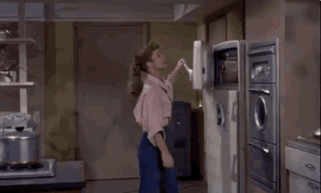 a woman in a pink shirt is standing in a kitchen with her fridge open .