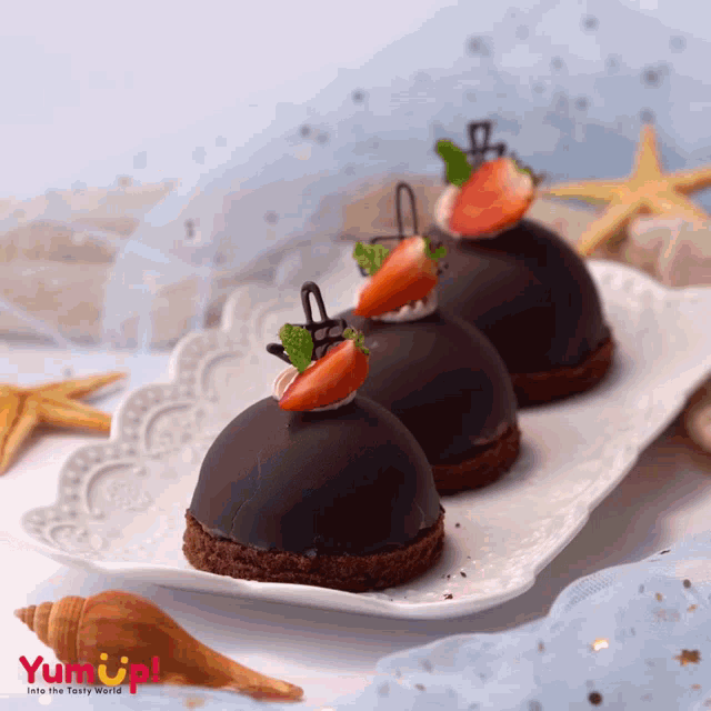 three chocolate desserts with strawberries on top are on a white plate that says yum up !
