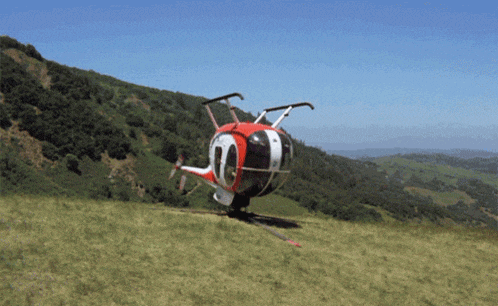 a red and white helicopter is on a grassy hillside