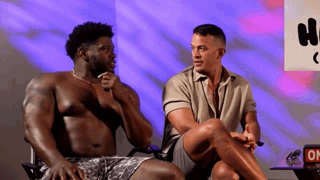 two shirtless men are sitting next to each other in front of a sign that says " on "
