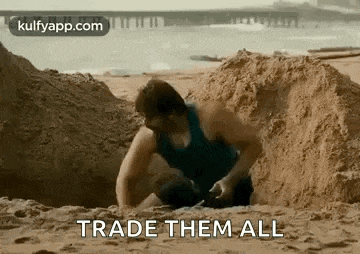a man is digging a hole in the sand on a beach and says `` trade them all '' .