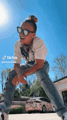a woman wearing sunglasses and a white t-shirt is kneeling down in front of a car that has the word tiktok on it