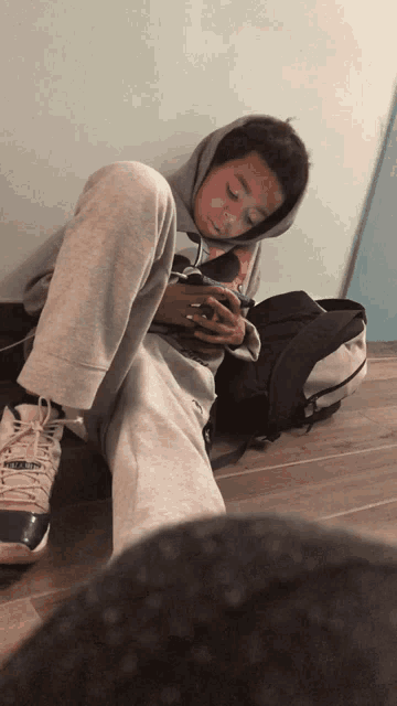 a boy wearing a hoodie and sweatpants is sitting on the floor with his legs crossed