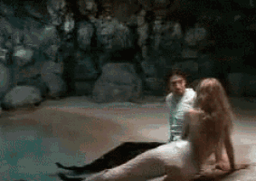 a man and a mermaid are sitting next to each other on a rock in a cave .