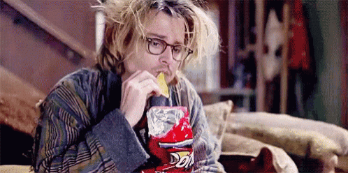 a man is sitting on a couch eating a bag of doritos .