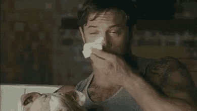 a man is holding a cat in his arms and wipes his face with a napkin .