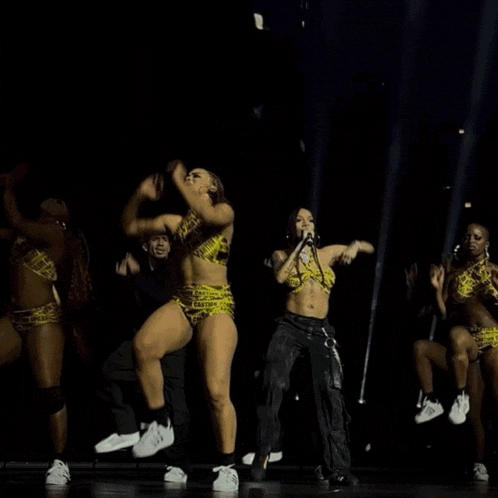 a group of dancers are performing on a stage with a man singing into a microphone behind them