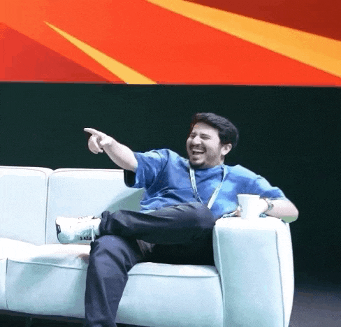 a man in a blue shirt is sitting on a white couch and pointing