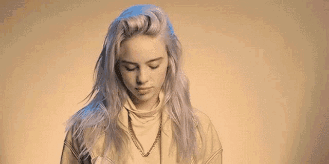 billie eilish is wearing a turtleneck sweater and a necklace .