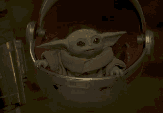 a baby yoda is sitting in a helmet with a red cushion