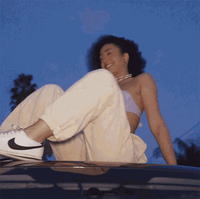 a woman wearing nike shoes sits on top of a car