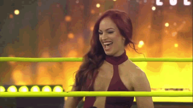 a woman in a red dress is standing in a wrestling ring laughing .