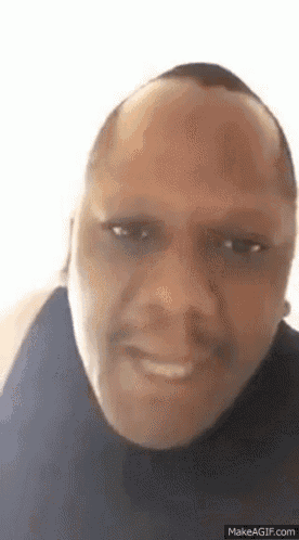 a man with a bald head is smiling and looking at the camera while wearing a black shirt .