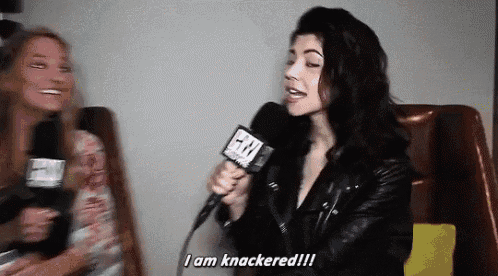 a woman in a leather jacket is holding a microphone and saying i am knackered !!!