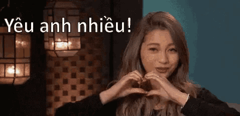a woman is making a heart with her hands in front of a sign that says yêu anh nhiều .