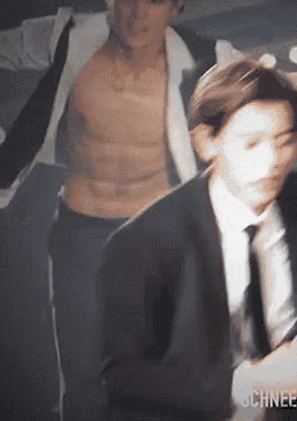 a shirtless man in a suit and tie is being followed by another man in a suit