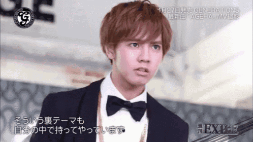 a young man in a tuxedo with a bow tie and a necklace is on a tv screen