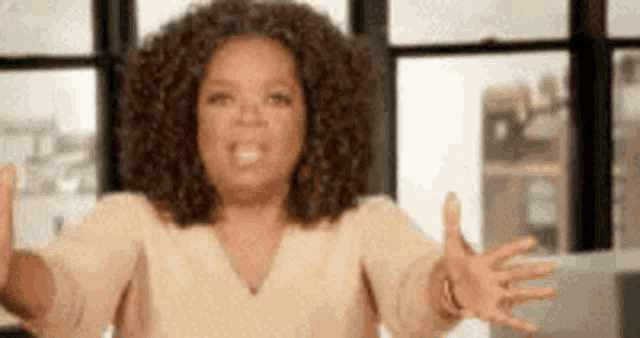 oprah winfrey is standing in front of a window with her arms outstretched and smiling .