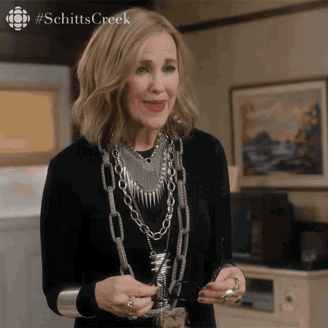 a woman wearing a black shirt and silver jewelry is holding a pair of glasses with the hashtag schitts creek on the top