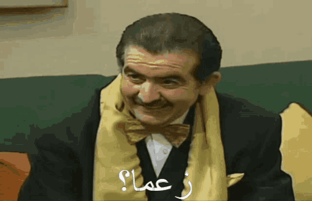 a man wearing a bow tie and a yellow scarf says " z oma " in arabic