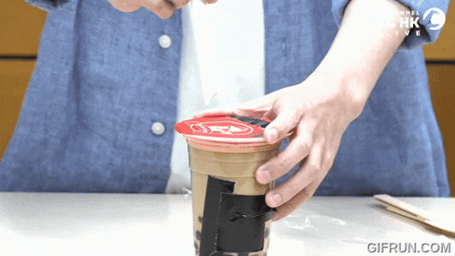 a person is opening a cup with a red lid that says hk