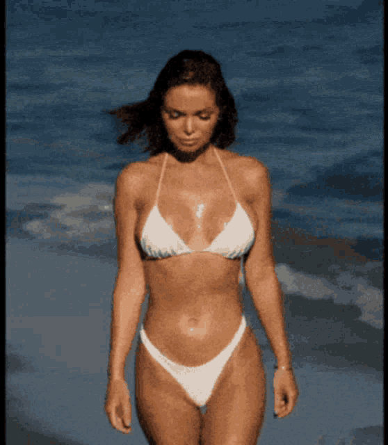 a woman in a white bikini is walking on a beach