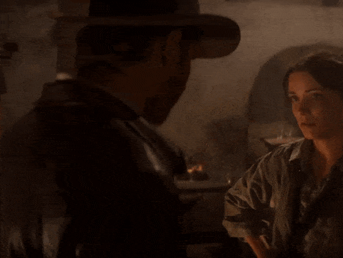a close up of a man wearing a hat and smoking a cigarette in a dark room .