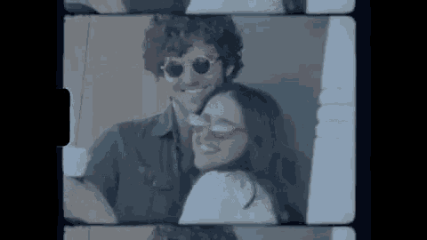 a man and woman wearing sunglasses are standing next to each other and smiling .