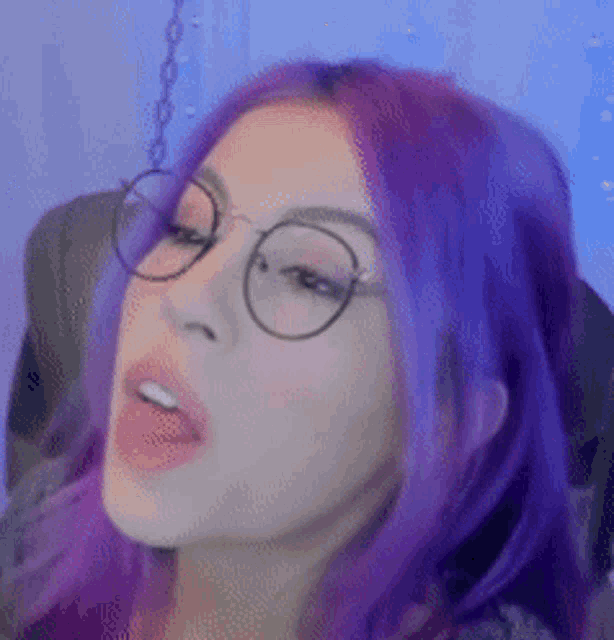 a woman with purple hair and glasses is making a face .
