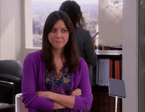 a woman wearing a purple sweater stands with her arms crossed
