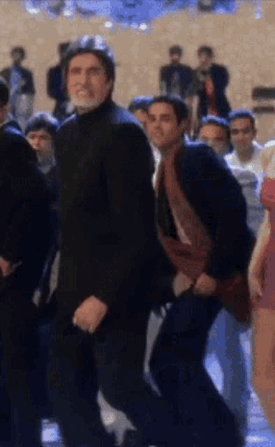 a man in a black suit is dancing in a crowd of people