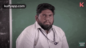 a man with a beard is sitting in front of a green chalkboard .