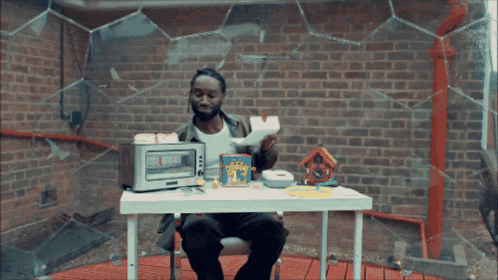 a man is sitting at a table with a toaster oven and a box of popcorn