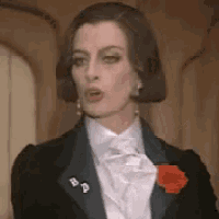 a woman is wearing a tuxedo and a white shirt with a red rose in her pocket .