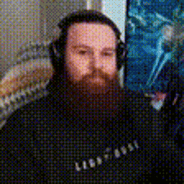 a man with a beard wearing headphones is sitting in front of a microphone .