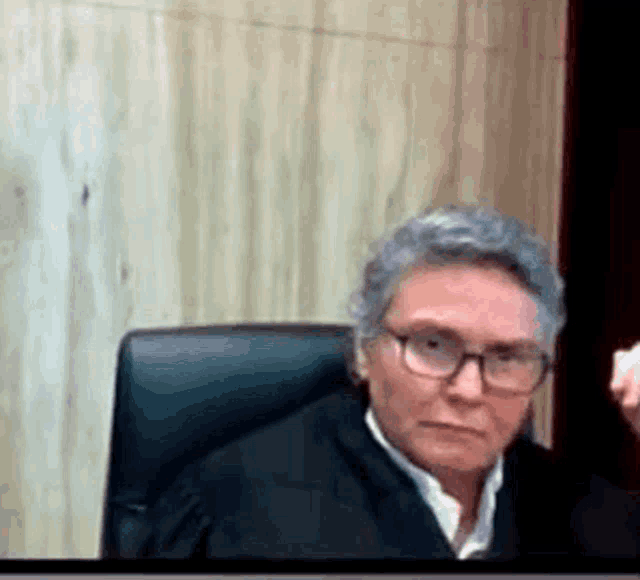 a woman in a judge 's robe and glasses is sitting in a courtroom .