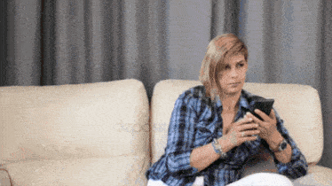 a woman sits on a couch looking at her cell phone