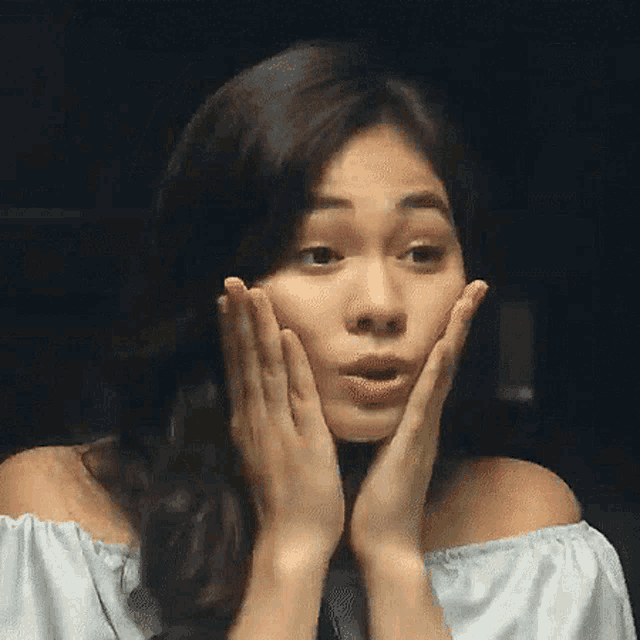 a woman is touching her face with her hands and making a funny face .