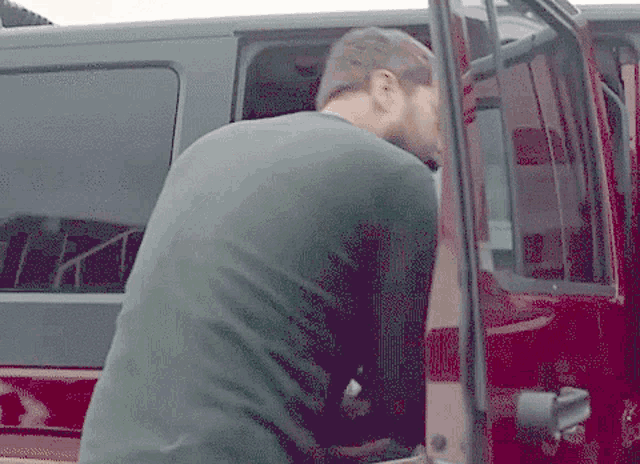 a man in a green shirt is getting out of a red car