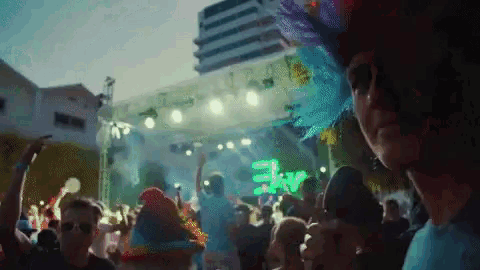 a man in a colorful hat stands in front of a stage with a green sign that says ekv